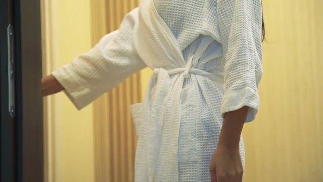 Back of young woman wrapped in white robe enters in sauna in spa salon