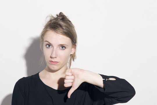 Young blonde woman with thumbs down sign, looking to camera, over a white background.