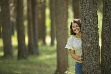A teenage girl stands at a tree in the Park and smiles.