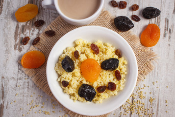 Cooked millet groats on white plate and cup of coffee with milk, healthy food and nutrition