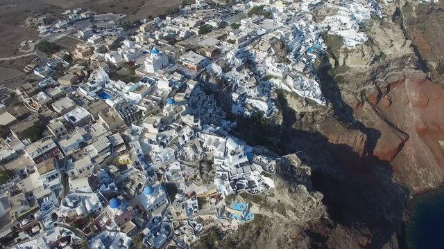 Aerial footage of Oia, Santorini - Famous white houses and blue domes on the edge of the cliff and blue lagoon.