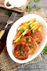 Minced meat cutlets and deep fried potatoes on a plate, a fork, a parsley leaves and burlap on old wood background. Cakes made with Turkey fillets and fried in vegetable oil. Recipe photo. Closeup