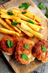 Turkey breast cutlets served with deep fried potatoes on cutting board and on an old wooden background. Cutlets prepared from minced meat and fried in vegetable oil in a frying pan. Closeup. Top view