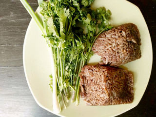 Khao kan chin, Local north thailand food of rice that is mixed with pork blood and steamed inside a banana leaf, serving with cucumber, onions and fried, dried chillies. Still life style.