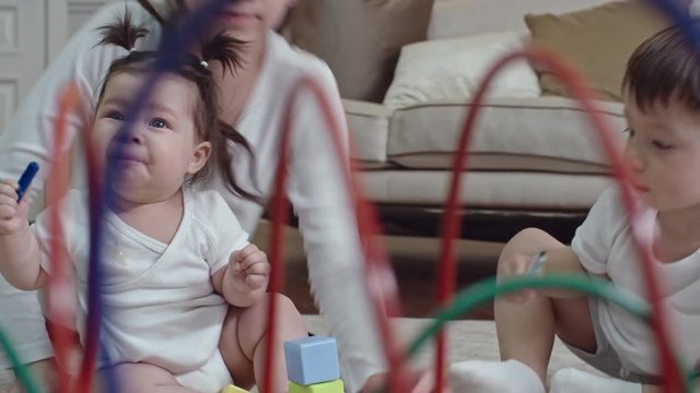 Little cute girl swallowing felt tip pen while her mom and brother drawing and then woman taking baby to clean up drool from her face