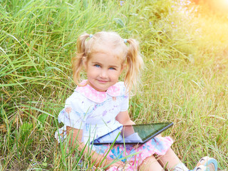 Little girl sitting in park on sunny day and play with tablet pc - 117957772