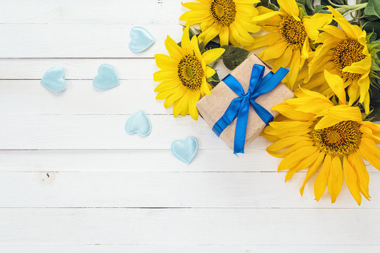 Background with a bouquet of yellow sunflowers, gift box and blu