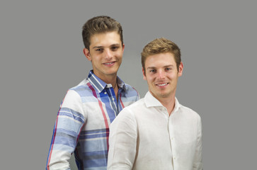 portrait of two beautiful young men smiling on grey background