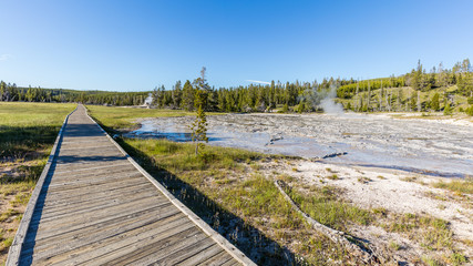 Fototapeta na wymiar Wooden walkway in the park leads to the one of the major geysers - Giant Geyser. It roars, splashes, steams. Upper Geyser Basin, Yellowstone National Park, Wyoming