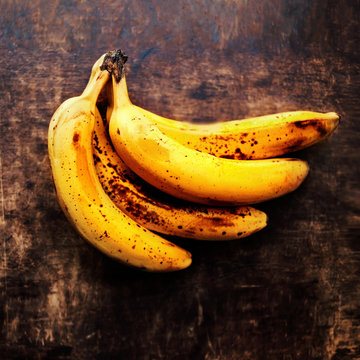 A branch of rotten ripe bananas on vintage wooden background. Ov