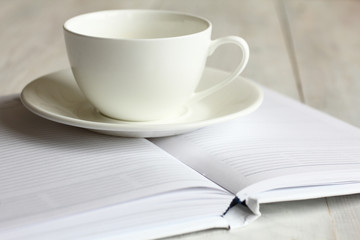 the Cup and saucer on the open book on wooden background.Monochrome