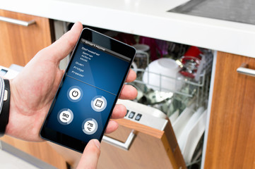 Man turns on the dishwasher by smartphone application.