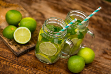 Fresh drink lemonade mojito in mason jar on wooden background. Mojitos with mint leaves, lime and ice. View from above.