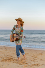 Silhouette of beautiful elegant female with guitar at the beach, sunset outdoors background.