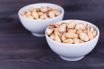 Salted pistachios in a bowl on dark wooden background. Space for text