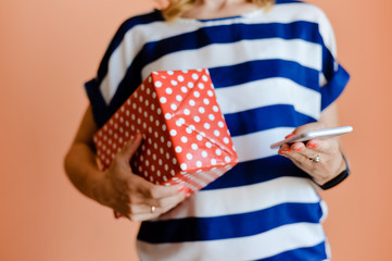 Closeup excited young woman holding present box using smartphone, light red orange background