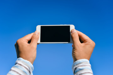 Blue sky with person hand using touch smartphone, sunny background