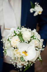 The groom holds a bridal bouquet in hand. A bouquet of flowers from lilies and white roses.