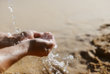 Fototapeta premium Person holding hands in splashes of water, sunny sandy outdoors background