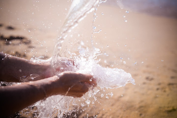 Closeup on hands holding water, sunny beach outdoors background