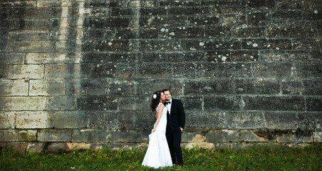 Happy couple stands behind an old stone wall