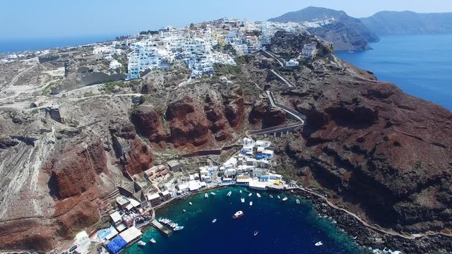 Aerial footage of Oia, Santorini - Famous white houses and blue domes on the edge of the cliff and blue lagoon.