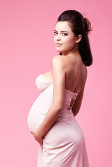 Pin up retro styled studio shot of a surprised pregnant woman. Photograph taken in studio on a pink, vibrant background with copy space.