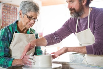 Male potter assisting female potter while making pot