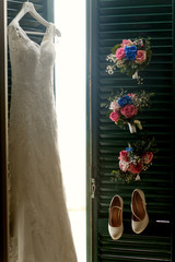 Sun shines through the green doors on which hang dress, shoes an