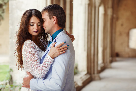 Bride Holds Her Hands Over Broad Groom's Shoulders Dressed In Bl