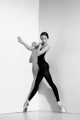 Ballerina in black outfit posing on pointe shoes, studio background.