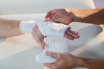 Physiotherapist putting bandage on male patient hand