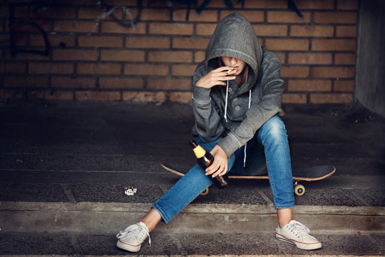Teen girl holding a beer bottle and smokingon steps