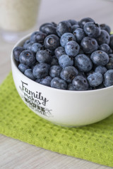 White bowl with Family text full of fresh blueberries on a green cloth and a bright wooden table.