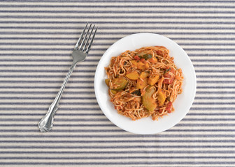 Angel hair pasta with zucchini and spinach on a plate atop a striped tablecloth.