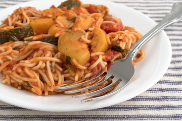 Angel hair pasta with zucchini and spinach on a plate atop a striped tablecloth.