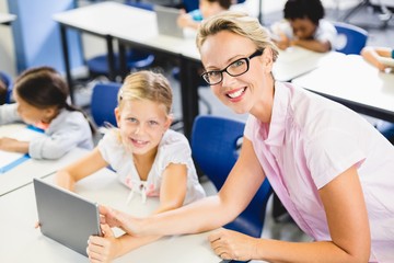Schoolgirl and teacher using digital tablet in classroom
