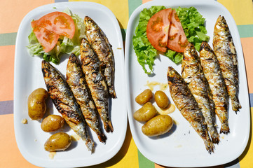 Top view on grilled sardines plate with potato on the table background, closeup flat lay