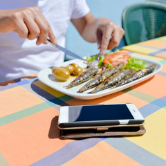 Top view on cellphone and grilled fish with potato on the table background, closeup