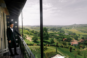 Smiling brunette man in black tuxedo stands on the balcony and a