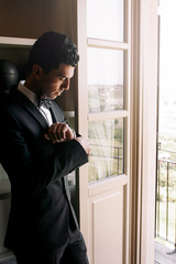 Fototapeta premium Brunette man adjusts his sleeves standing before a bright window