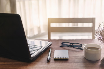 Laptop and cup of coffee with sunlight on desk office