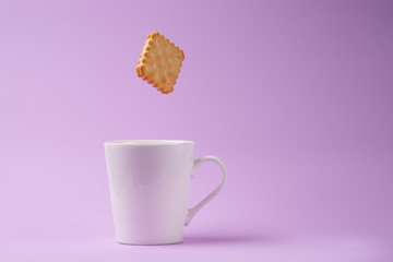square sandwich cracker falling to coffee cup on color backgroun