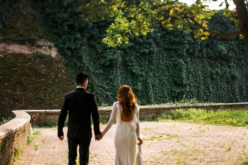 Fototapeta premium Man in black suit holds tender woman's hand walking around the g