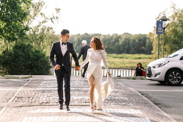 Obraz premium Stylish wedding couple walks across the pedestrian in a sunny da
