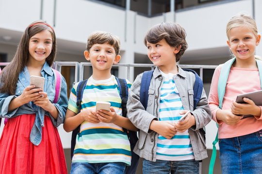 Kids holding phone and tablet standing on school 