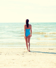 young woman in swimsuit walking on beach