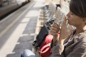 femme assise qui allume une cigarette sur un quai de gare 
