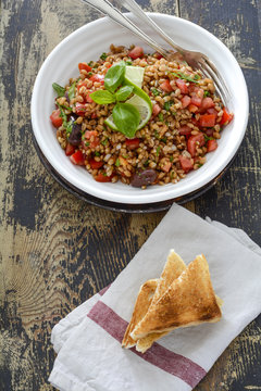 Emmer wheat with black olives, tomato, lime, basil and parsley on plate, toast bread