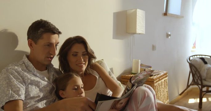 Happy smiling caucasian family laying in bed, mother, father and daughter reading magazine